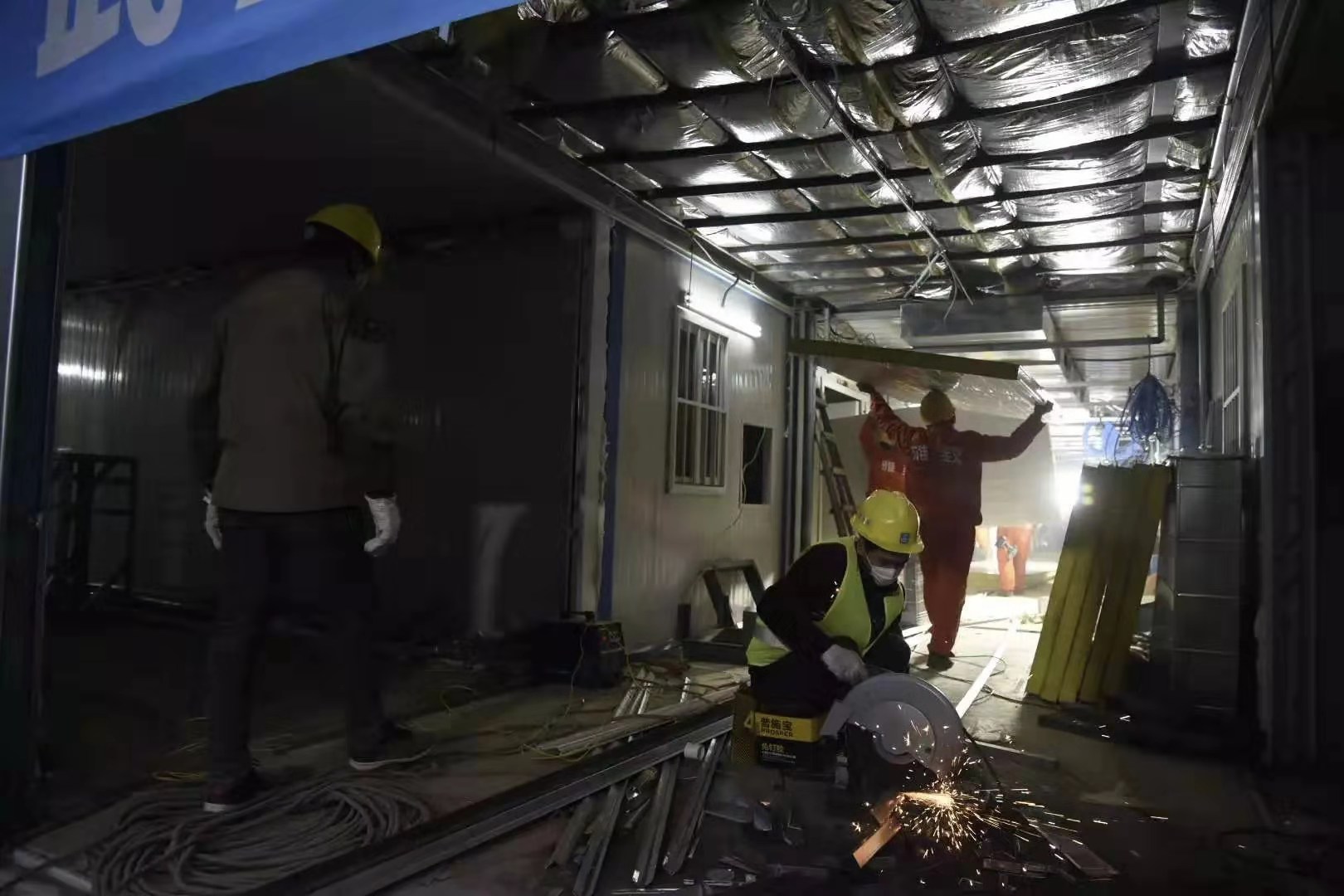 為了優(yōu)質(zhì)高效地推進火神山醫(yī)院項目實施，1月25日項目啟動之時，中建三局現(xiàn)場成立了6支、322名員工組成的青年突擊隊，青年員工們紛紛請戰(zhàn)，并且從全國各地“逆行”馳援武漢參戰(zhàn)。為保證施工進度，青年突擊隊制定了“小時制”作戰(zhàn)地圖，搭建了工程“大數(shù)據(jù)”，并采取24小時輪班作業(yè)，突擊隊員不畏疫情兇險，精誠團結(jié)、通力合作，很多人不眠不休沖鋒在施工一線。圖為2月1日17時30分，火神山醫(yī)院一號樓，施工人員在進行室內(nèi)裝潢。