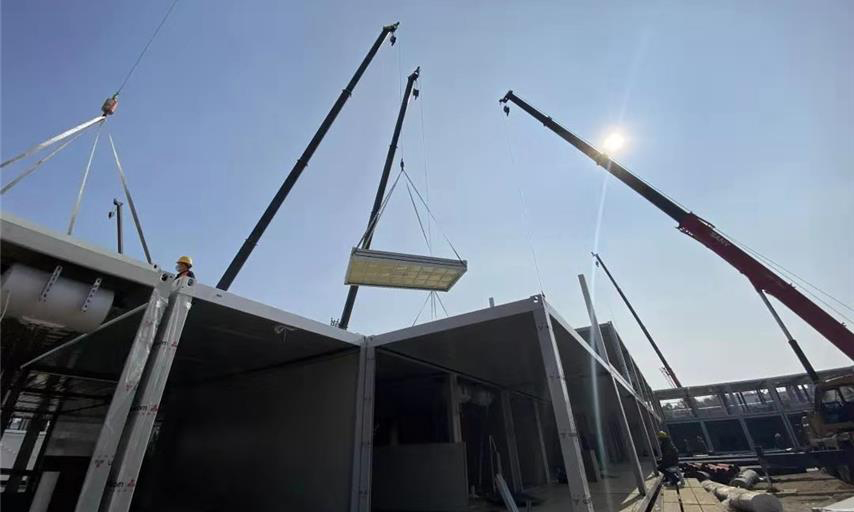 截至1月30日中午12時，武漢火神山醫院項目場地平整、砂石回填、HDPE膜鋪設全部完成，基礎混凝土澆筑完成95％；集裝箱板房進場、改裝、吊裝正快速推進。管線溝槽開挖、埋設級回填完成50％；污水處理間設備吊裝完成，管道安裝完成60％；調蓄水池HDPE膜開始鋪設。圖為住院樓板房吊裝現場。