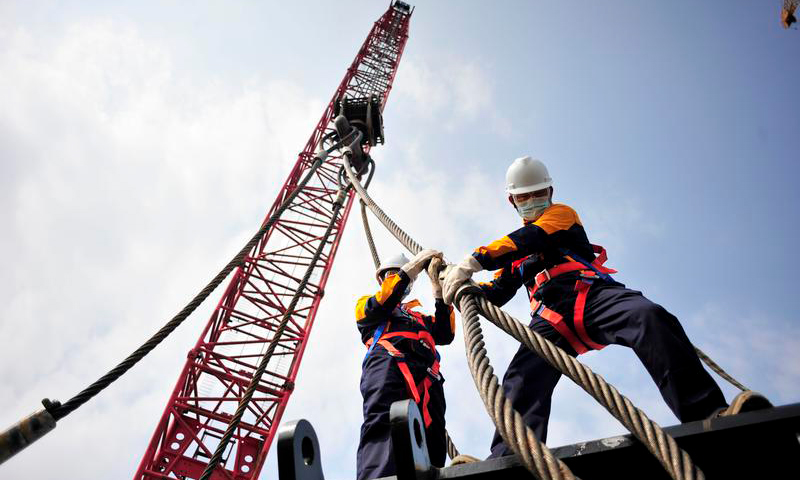 近日，在中國海油海油工程建造事業部青島場地，員工們頭頂烈日，不畏高溫天氣正在加緊進行一臺2000噸“巨無霸”履帶吊的組裝工作，以為后續加拿大LNG核心工藝模塊大型、超高結構物的高效吊裝爭取時間。圖為組裝作業現場，施工人員正在進行掛扣作業。