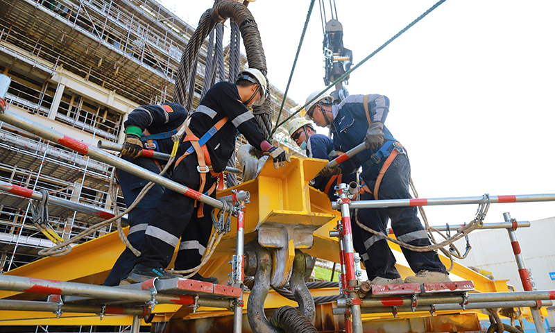 為有效緩解這一局面，高效推動項目施工進度，建造事業部青島公司在提升精細化管理能力和水平上下功夫。通過成立甲板片臨時倒運小組，提前疏通車道障礙，讓原本滯緩的場地運輸工作高效運轉。圖為Mini E-House（電氣間）吊裝作業人員合力安裝吊裝鎖具。