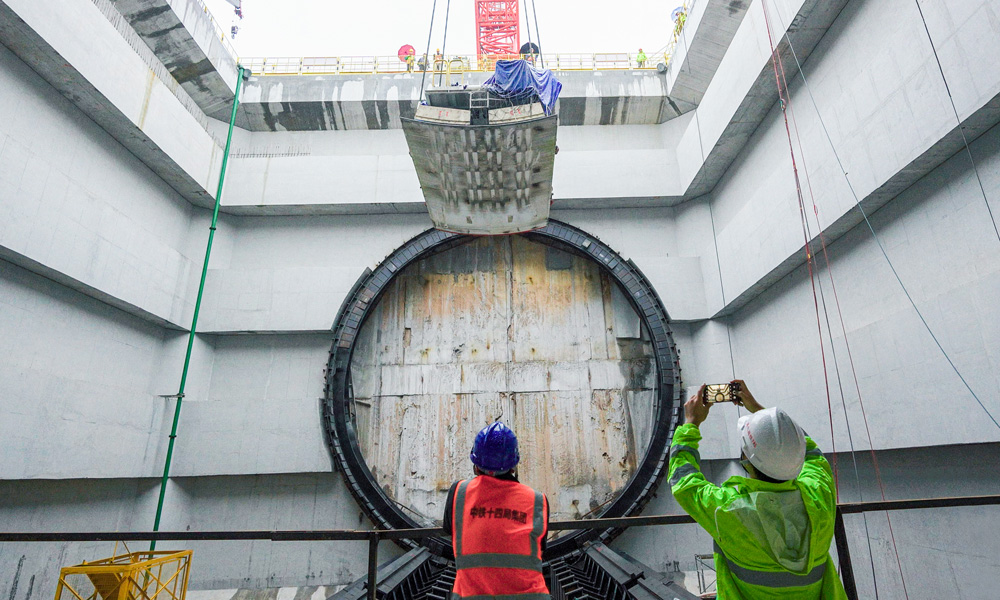 為隧道建設(shè)量身定制的盾構(gòu)機(jī)“英雄號(hào)”全長134米，開挖直徑14.8米。連日來，盾構(gòu)機(jī)主驅(qū)動(dòng)、刀盤、拼裝機(jī)等已運(yùn)輸下井、完成組裝，后期將進(jìn)行盾構(gòu)機(jī)管線連接和整機(jī)調(diào)試工作，即將開始盾構(gòu)隧道掘進(jìn)。圖為施工人員在現(xiàn)場緊盯盾體下井定位組裝。